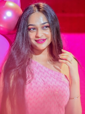 A young woman applying vibrant pink lipstick with a joyful smile.
