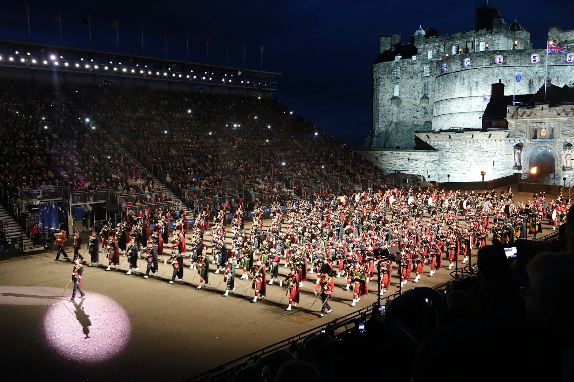 A dramatic evening scene with flags waving and soldiers marching in formation during the Poole Military Tattoo event.