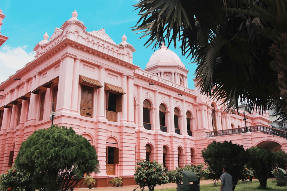 a large pink building sitting next to a lush green park