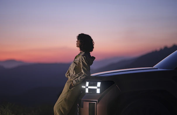 A driver assisting an elderly passenger into a comfortable vehicle at sunset