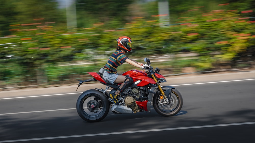 a man riding a red motorcycle down a street