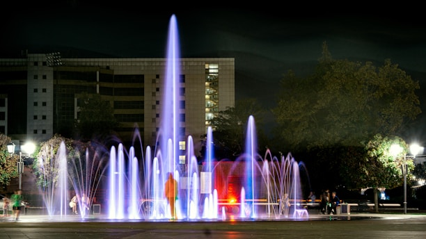 A modern water fountain with dynamic water flows illuminated by soft lights at dusk.