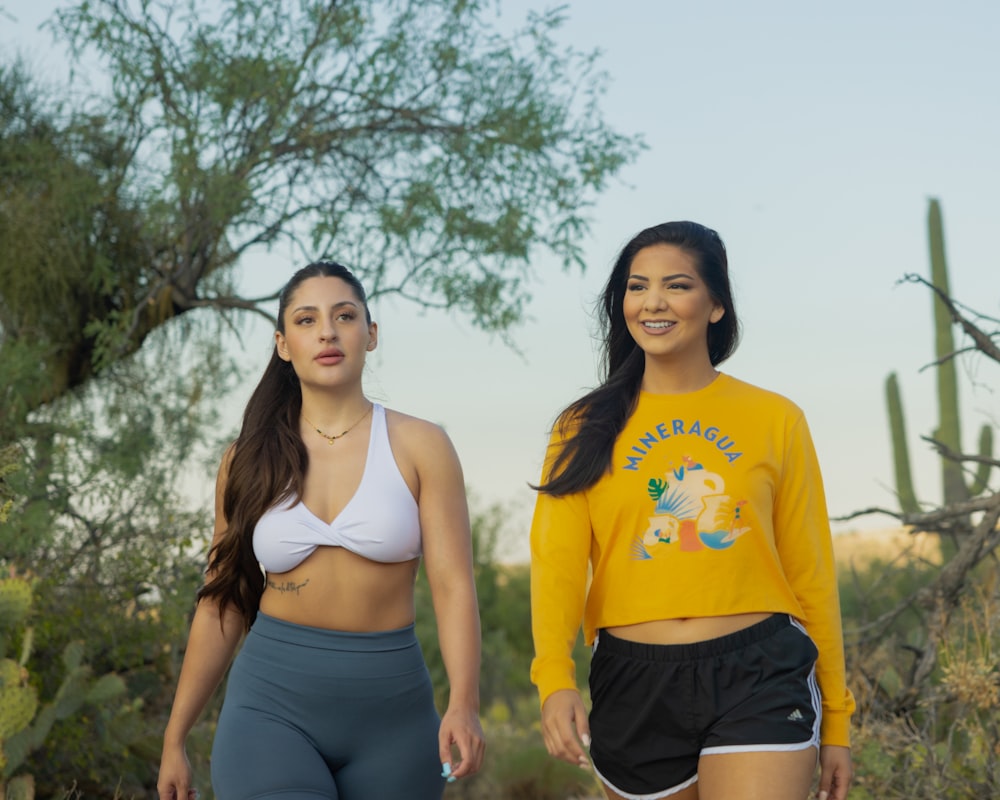 two women walking in the desert with cactus trees in the background