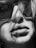 A close-up black and white photograph of a person's face, focusing on their lips and nose. The person is wearing dark oversized sunglasses and strands of hair partially cover the face, adding a dramatic effect.
