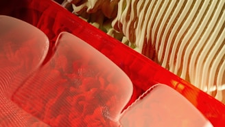 Abstract shapes and textures dominate the scene, featuring a combination of smooth red surfaces and intricate, wavy patterns. The interplay between light and shadow enhances the three-dimensional quality of the objects, creating a dynamic and visually intriguing composition.