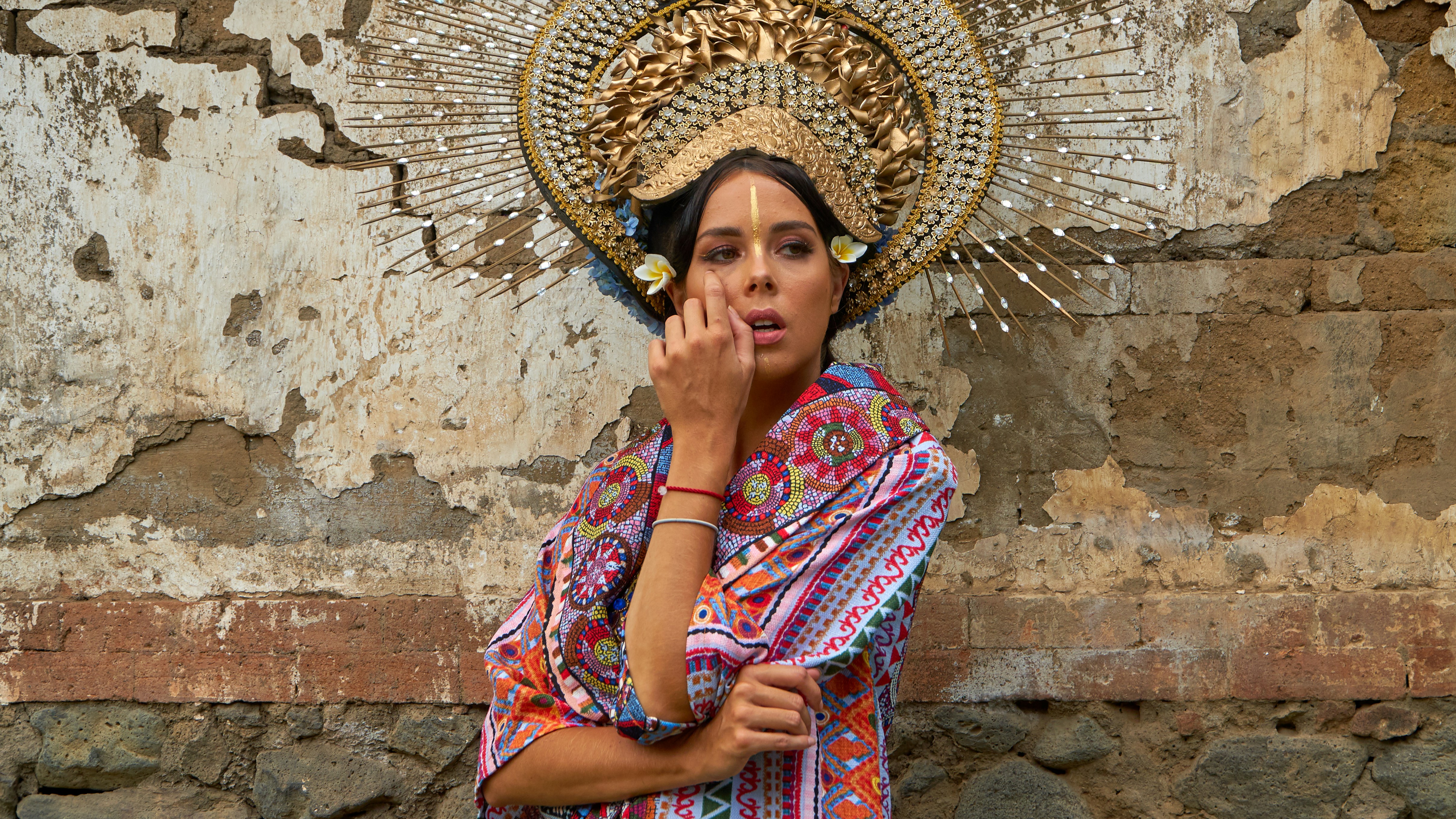 a woman in a colorful dress standing in front of a stone wall