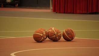 three basketballs sitting on a basketball court with a red curtain in the background