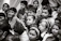 A group of children gather closely together, attentively observing something. Their expressions vary from curiosity to wonder. The scene is in black and white, creating a timeless feel.