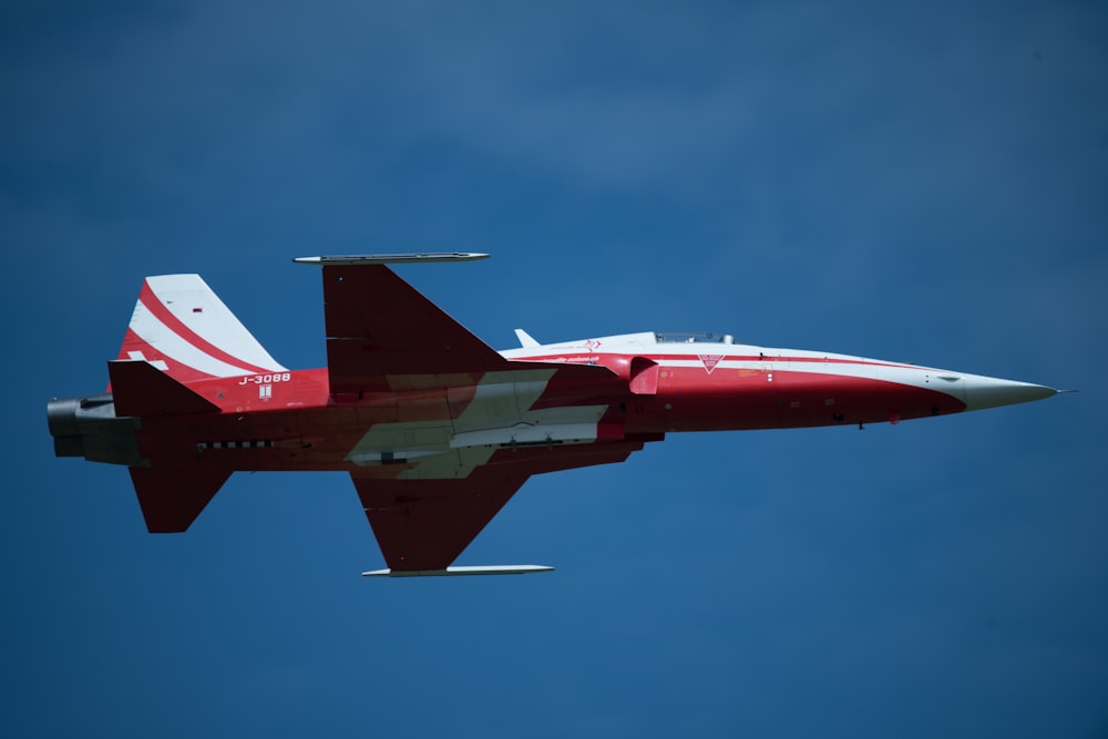 a red and white jet flying through a blue sky