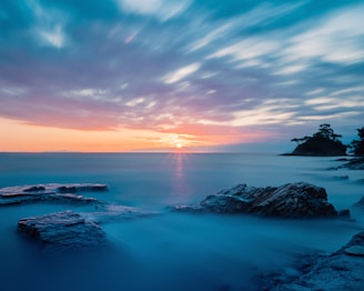the sun is setting over the ocean and rocks