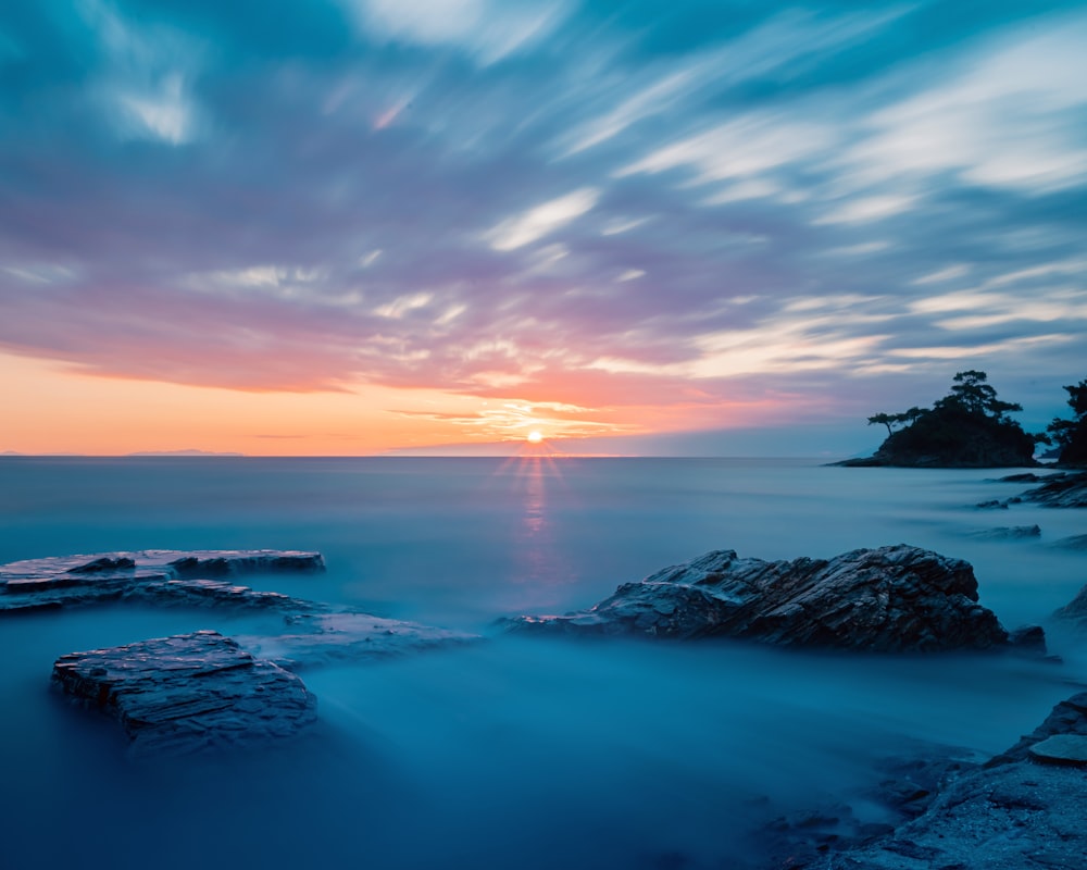 the sun is setting over the ocean and rocks