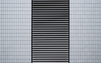 A modern architectural facade featuring a grid of small, white, textured tiles flanking a central black panel composed of horizontal slats.