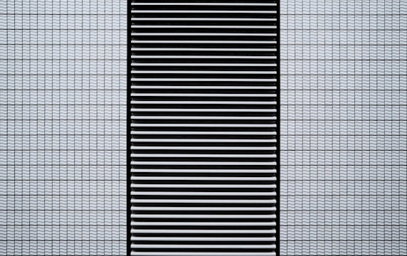 A modern architectural facade featuring a grid of small, white, textured tiles flanking a central black panel composed of horizontal slats.