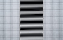 A modern architectural facade featuring a grid of small, white, textured tiles flanking a central black panel composed of horizontal slats.