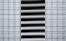 A modern architectural facade featuring a grid of small, white, textured tiles flanking a central black panel composed of horizontal slats.