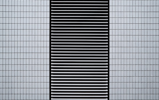A modern architectural facade featuring a grid of small, white, textured tiles flanking a central black panel composed of horizontal slats.