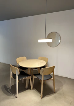 Minimalist steel and wood chairs arranged around a glass dining table in a bright room