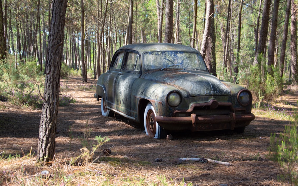 an old car is parked in the woods