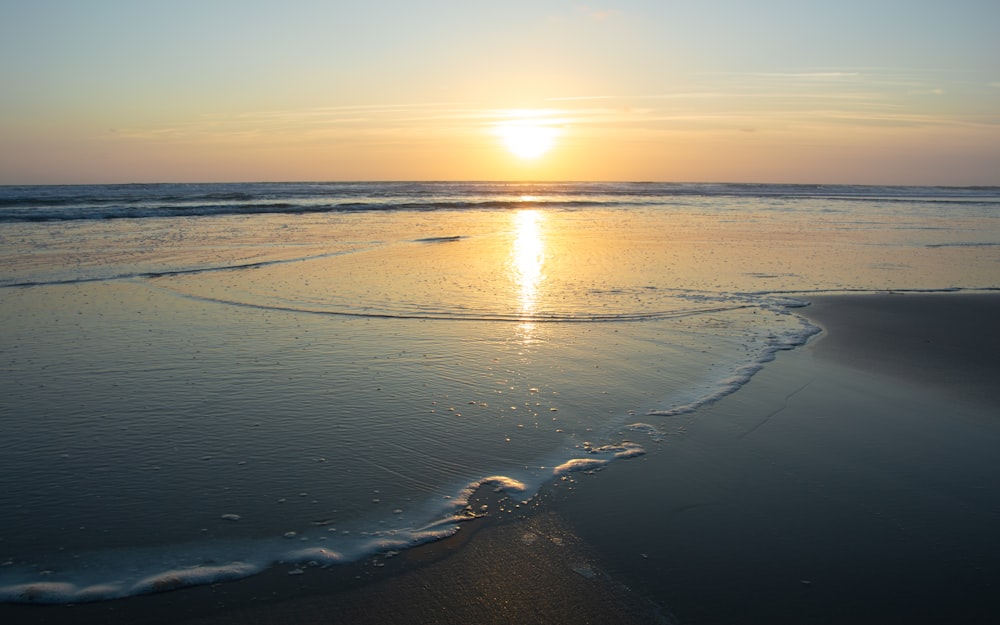 the sun is setting over the water at the beach