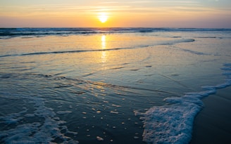 the sun is setting over the water at the beach
