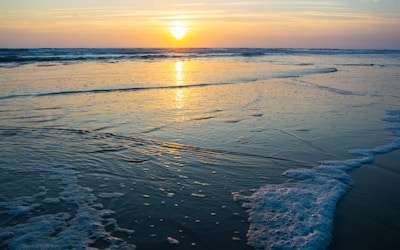 the sun is setting over the water at the beach