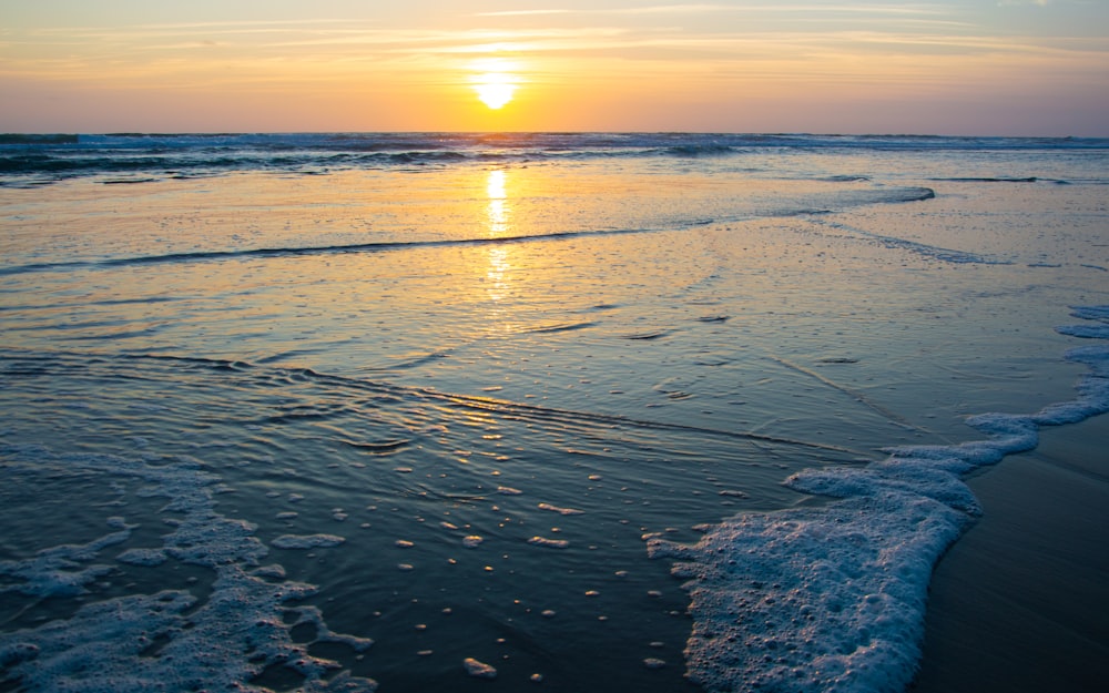 the sun is setting over the water at the beach