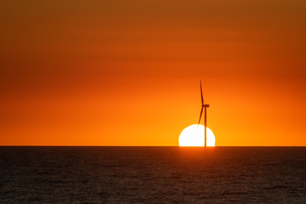 the sun setting behind a wind turbine in the ocean
