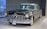 A classic vintage car with a polished black exterior and chrome detailing stands in an indoor showroom. The car has a distinctive front grille, round headlights, and white-walled tires, evoking a sense of elegance and luxury.