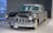 A classic vintage car with a polished black exterior and chrome detailing stands in an indoor showroom. The car has a distinctive front grille, round headlights, and white-walled tires, evoking a sense of elegance and luxury.
