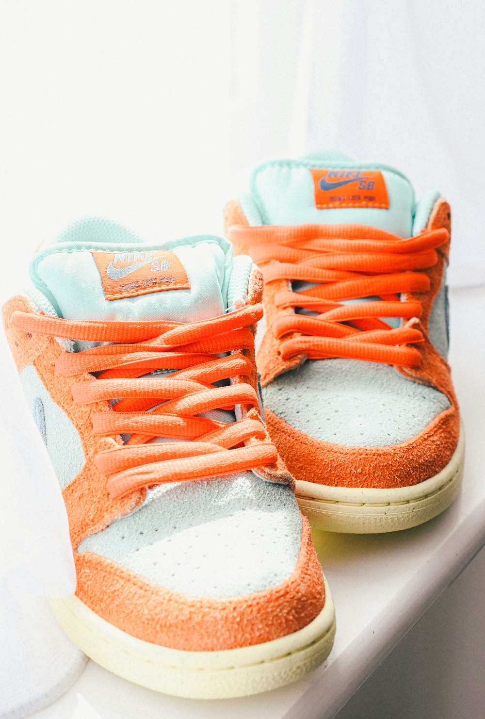 a pair of orange and white sneakers sitting on a ledge