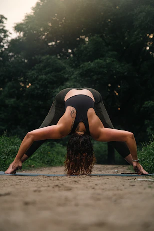 Woman practicing yoga outdoors on a green Orygen mat surrounded by lush forest.