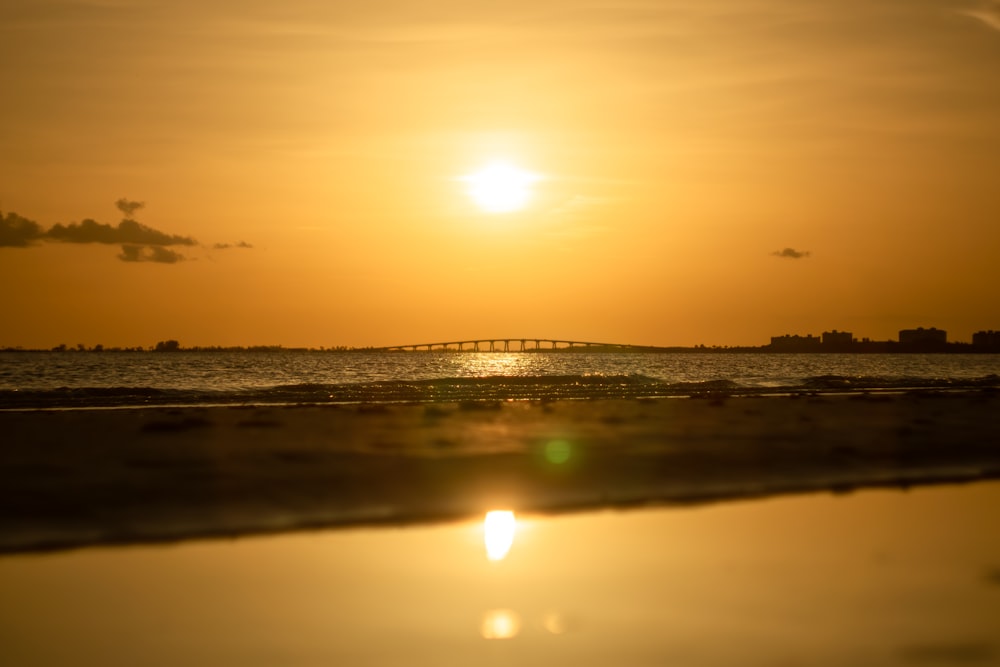 the sun is setting over the ocean with a bridge in the distance
