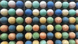A grid of colorful basketballs arranged in an organized manner, showcasing a variety of hues such as blue, green, orange, and yellow. Each basketball is positioned within a compartment, creating a pattern across multiple rows and columns.