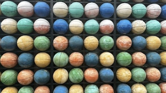 A grid of colorful basketballs arranged in an organized manner, showcasing a variety of hues such as blue, green, orange, and yellow. Each basketball is positioned within a compartment, creating a pattern across multiple rows and columns.
