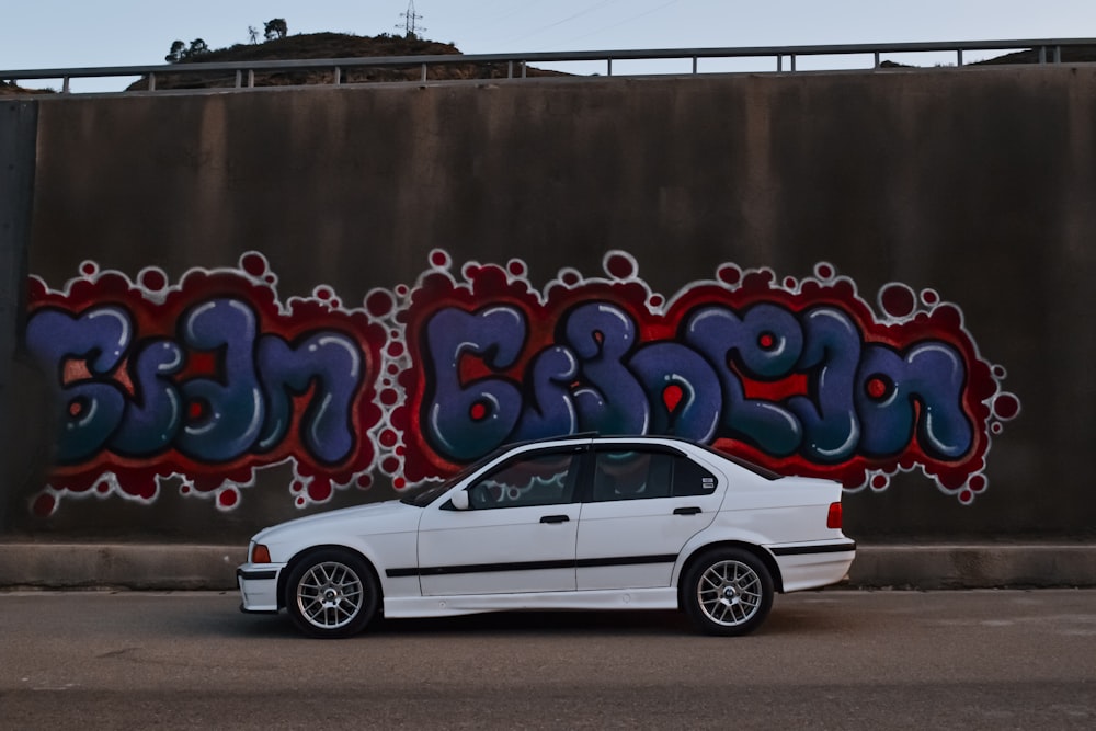 a white car parked in front of a graffiti covered wall