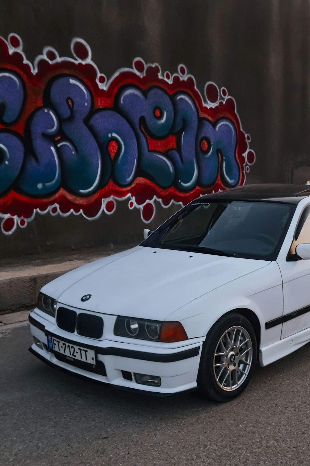 a white car parked in front of a graffiti covered wall