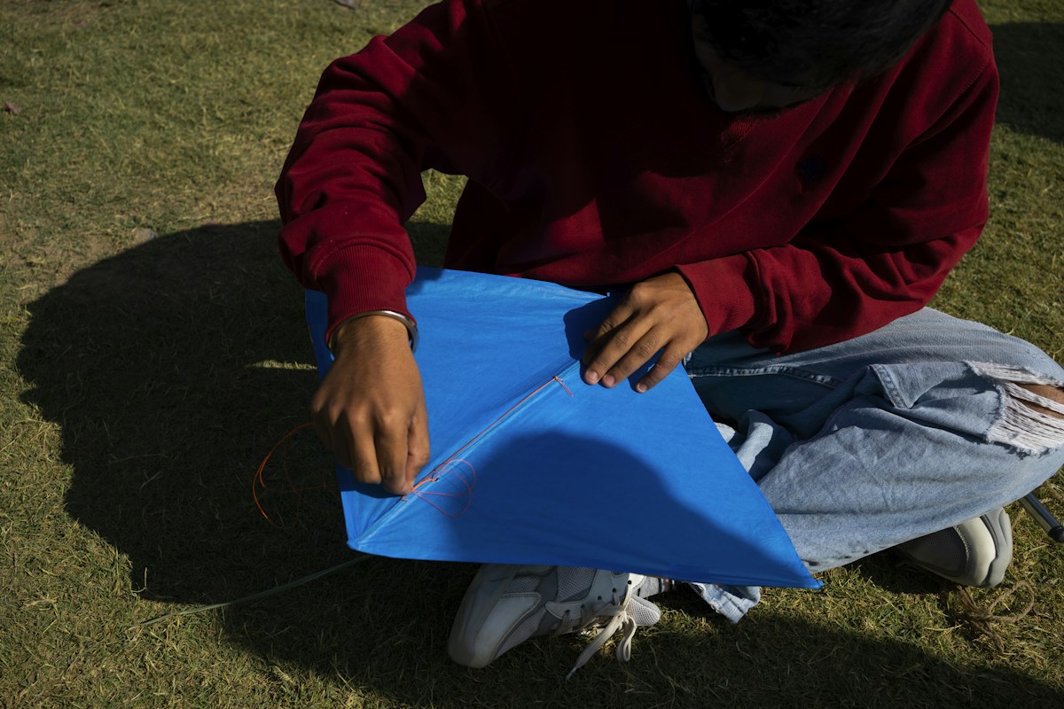 Man sitting on grass holding a blue kite, ideal for elementary school field day activities and volunteer coordination ideas.