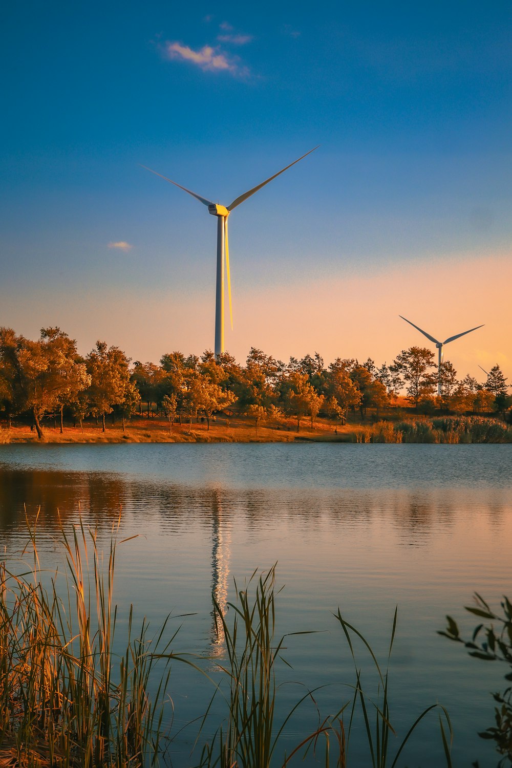 two wind turbines are seen in the distance over a lake