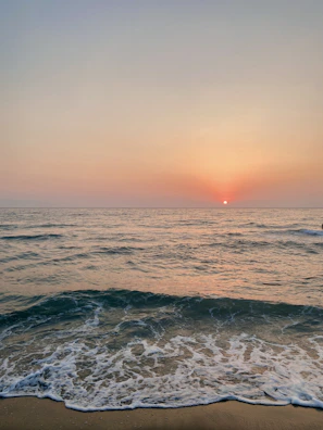 A serene coastal view with gentle waves and a pastel sky at sunset.