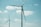 Two large wind turbines stand against a bright sky with scattered clouds. The blades of the turbines are clearly visible, adding to the sense of scale and height. The scene suggests a focus on renewable energy.