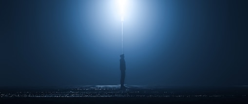 A moody black-and-white film still featuring a lone figure silhouetted against a foggy urban backdrop.