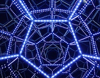 A geometric structure is composed of interconnected lines forming a complex pattern with bright, glowing blue lights. This intricate design creates an illusion of depth and symmetry.