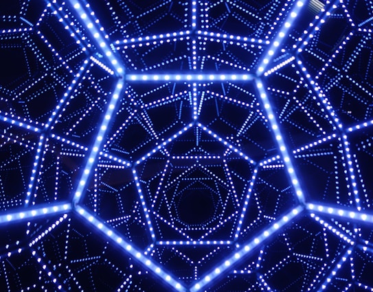 A geometric structure is composed of interconnected lines forming a complex pattern with bright, glowing blue lights. This intricate design creates an illusion of depth and symmetry.