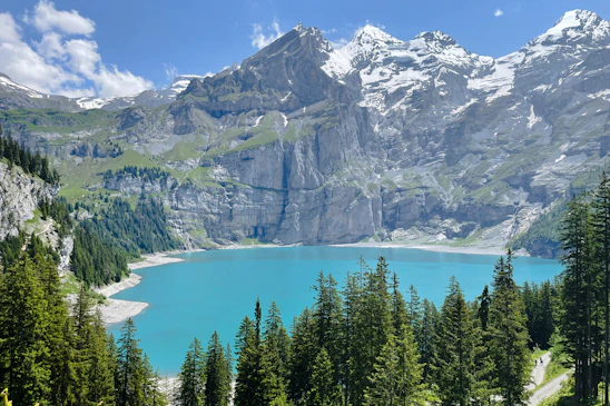 A crisp, wide-angle shot of a turquoise alpine lake framed by towering snow-capped peaks under a clear blue sky.