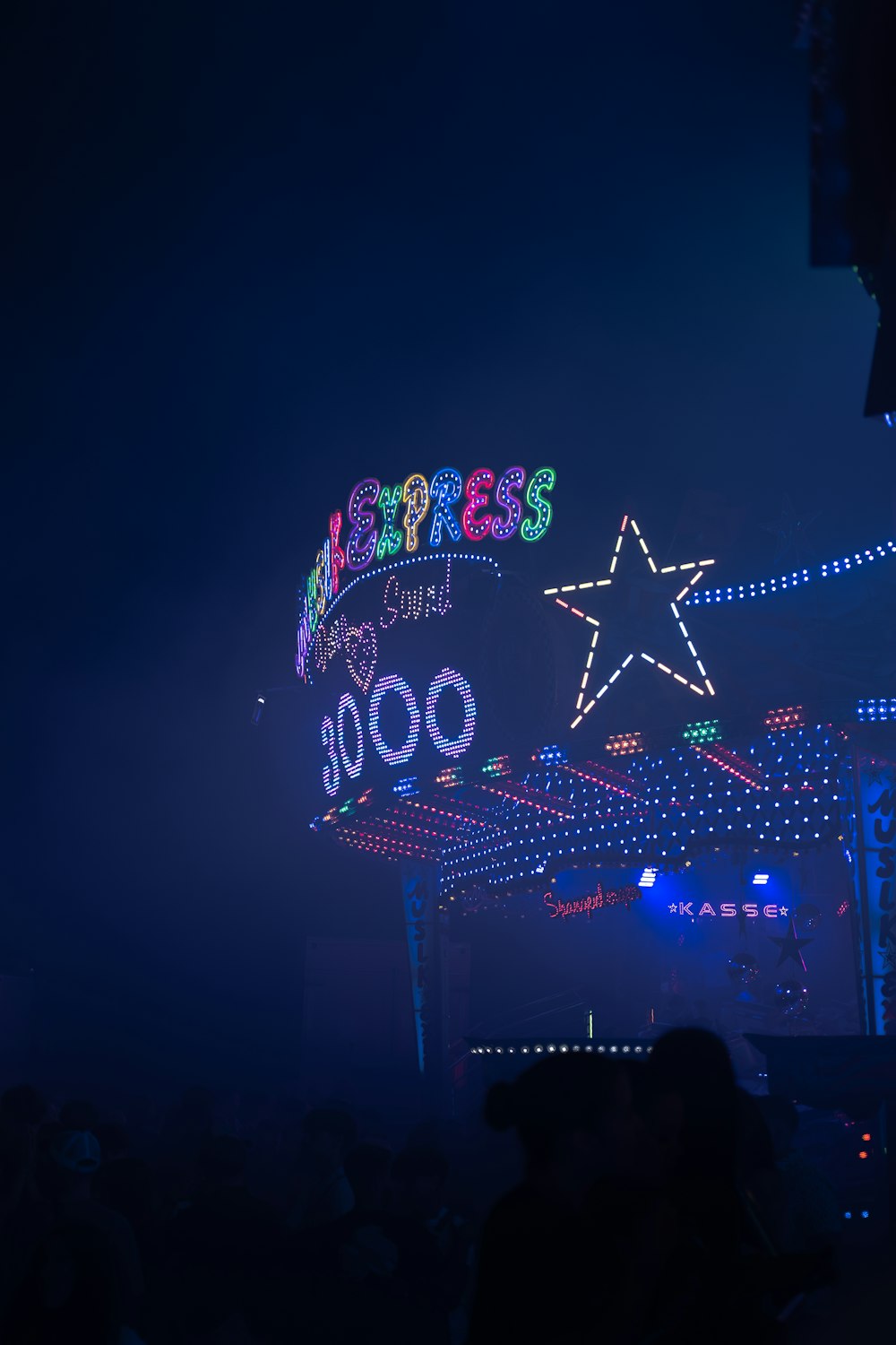 a crowd of people standing around a fairground at night