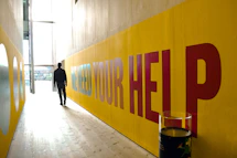 a man walking down a hallway next to a yellow wall