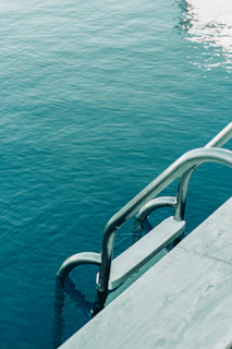 A vintage pool ladder emerging from crystal-clear water surrounded by lush greenery.