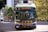 A public transit bus marked as 44 UBC EXPRESS is centered in the frame. The background includes urban elements such as buildings and traffic lights, while trees add a touch of greenery. The bus is painted with blue and yellow accents.