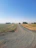 A wide shot of a smooth gravel rural road stretching into the distance with green fields on either side.