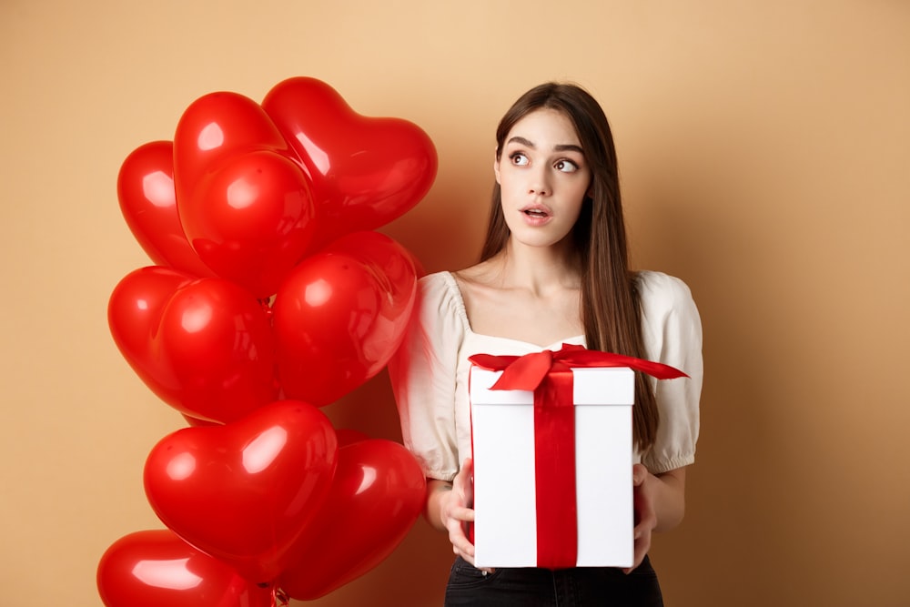 a woman holding a gift box and a bunch of balloons